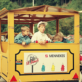 Ein gelber Waggon, in dem drei Kinder sitzen und durch die geöffnete Rückwand rausschauen