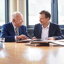 Walter Mennekes & Christopher Mennekes sitzen am Tisch und schauen sich lächelnd an