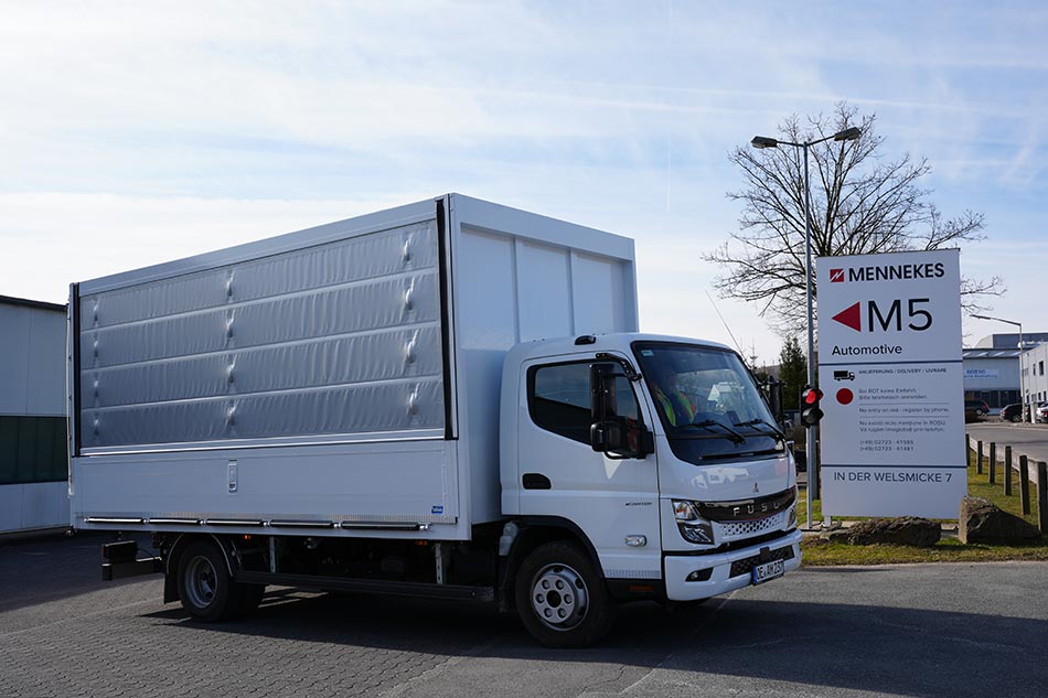 Ein weißer E-LKW von MENNEKES vor dem Eingang einer Lagerhalle