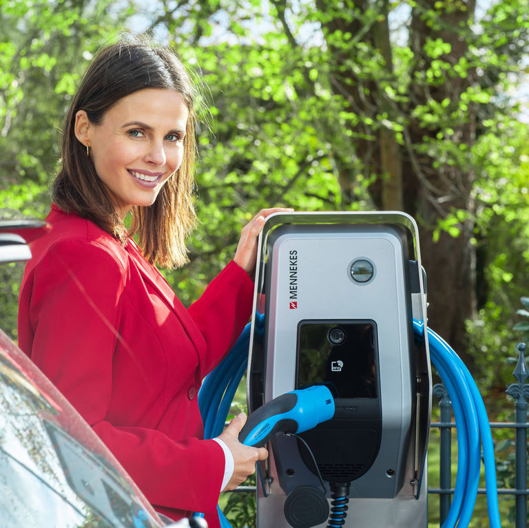 Frau mit Ladekabel und Wallbox mit Solarladefunktion