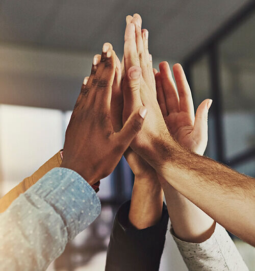 Unternehmenskultur Mehrere Hände unterschiedlicher Personen klatschen im Büro zu einem gemeinsamen High-Five.