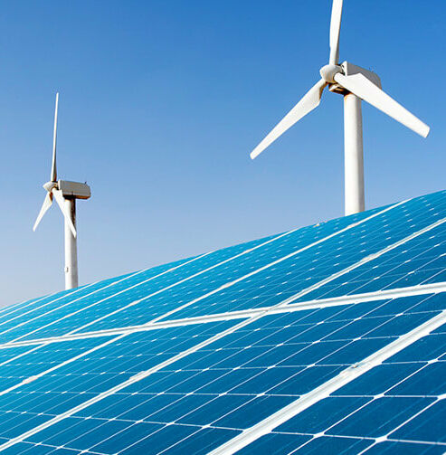 Produkte und Services für eine nachhaltigere Welt Großes Solarpanel vor Reihe weißer Windräder unter klarem blauem Himmel.